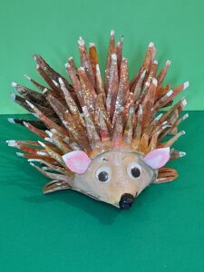 27) I added sme PVA glue and sprinkled glitter, which gave the hedgehog a sparkle, and paint the tips in white. Paint on a smiley mouth in black, and slight eyebrows.