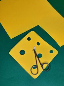 9) Cut out a square shape from a yellow piece of card and with a smaller scissors cut out different sized holes.