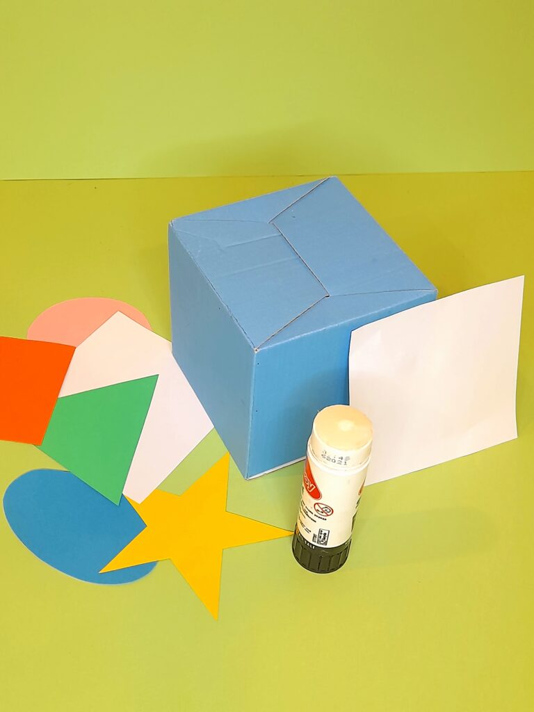 Getting the cube ready to stick on the shapes. White square paper covering the cube folds.